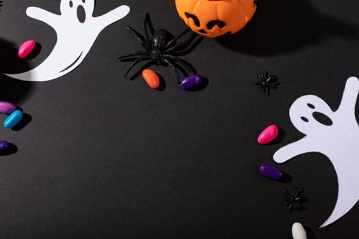 Composition of halloween decorations with black spider, ghosts and pumpkin on black background. halloween tradition and celebration concept.