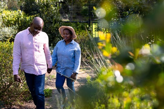 Happy african american senior couple holding hands outdoors. retirement lifestyle, spending time at home and garden.
