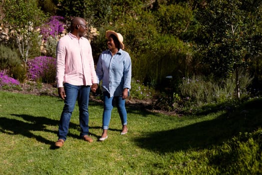Happy african american senior couple holding hands outdoors. retirement lifestyle, spending time at home and garden.