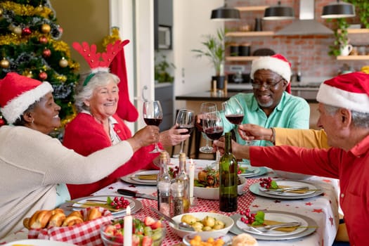 Diverse group of happy senior friends celebrating christmas with vine together at home. christmas festivities, celebrating at home with friends.