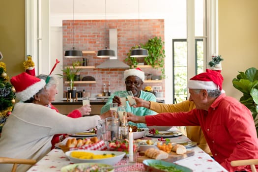 Diverse group of happy senior friends celebrating christmas together, toasting with juice. christmas festivities, celebrating at home with friends.