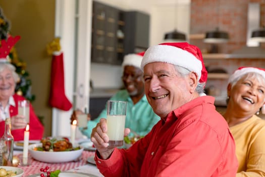 Happy caucasian senior man holding glass and celebrating christmas with diverse group of friends. christmas festivities, celebrating at home with friends.