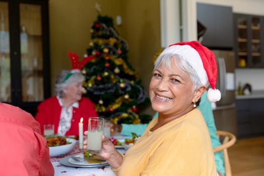 Happy mixed race senior woman holding glass and celebrating christmas with diverse group of friends. christmas festivities, celebrating at home with friends.