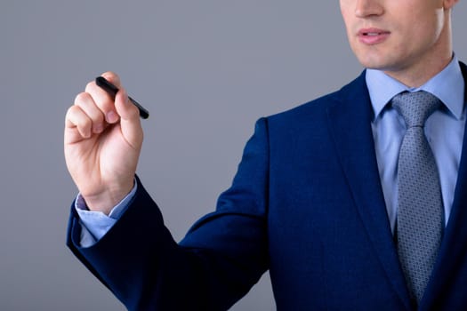 Midsection of caucasian businessman holding pen, isolated on grey background. business technology, communication and growth concept.