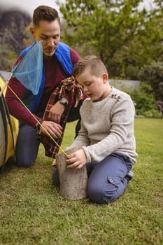 Caucasian father watching while his son setting up a tent in the garden. fatherhood and love concept