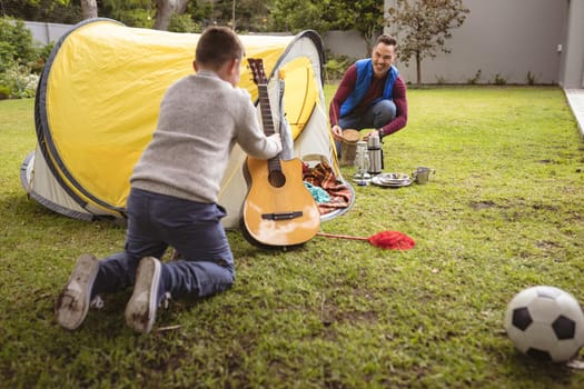 Caucasian father and son smiling while setting up a tent together in the garden. fatherhood and love concept