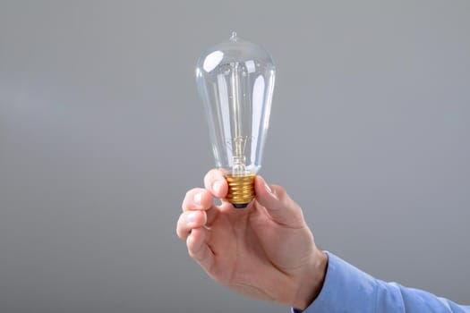 Midsection of caucasian businessman holding light bulb, isolated on grey background. business technology, communication and growth concept.