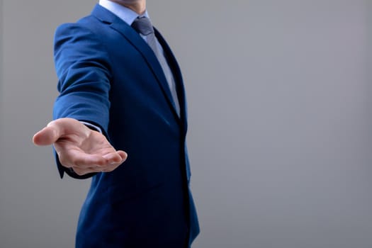 Midsection of caucasian businessman reaching his hand, isolated on grey background. business technology, communication and growth concept.