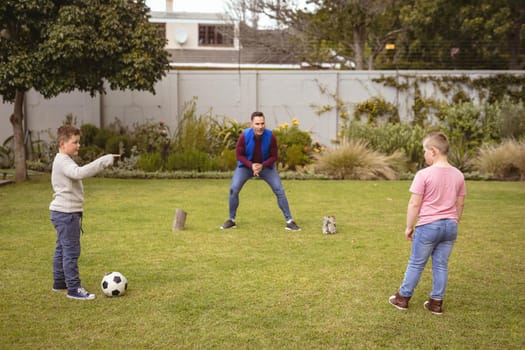 Caucasian father and two sons playing football together in the garden. fatherhood and love concept