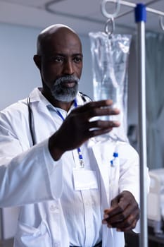 African american male doctor preparing iv drip bag on stand in hospital ward. medicine, health and healthcare services.