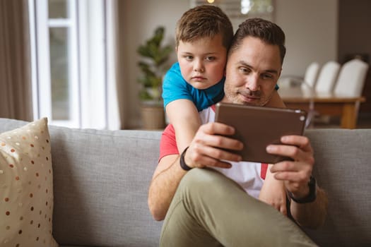 Caucasian father and son using digital tablet on the couch at home. fatherhood, technology and home concept