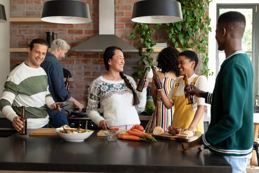 Group of happy diverse female and male friends drinking beer and cooking together in kitchen. socialising with friends at home.