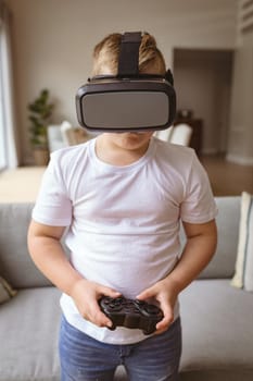 Caucasian boy wearing vr headset and holding gaming controller playing video games at home. gaming and entertainment concept