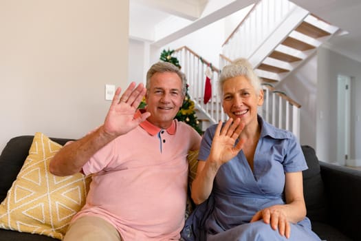 Happy caucasian senior couple having video call, waving to camera at christmas time. healthy retirement lifestyle at home.