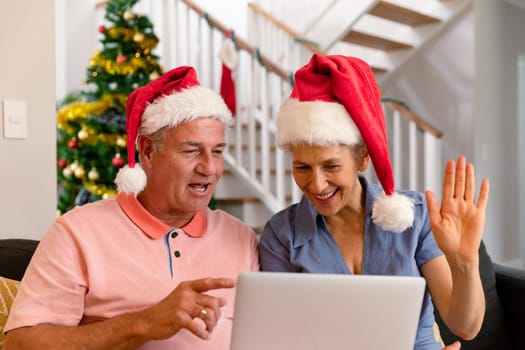 Happy caucasian senior couple wearing santa hat, using laptop, having video call at christmas time. christmas, festivity and communication technology.