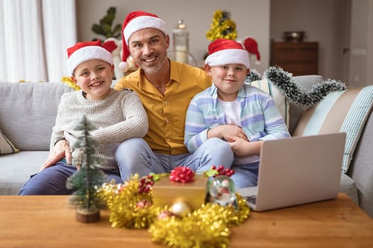 Portrait of caucasian father and two sons smiling while sitting at home during christmas. christmas festivity and celebration concept