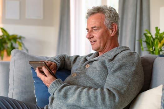 Happy caucasian senior man sitting on sofa and using tablet. active retirement lifestyle at home.