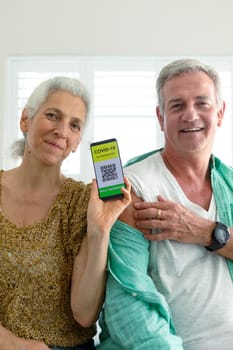 Smiling caucasian senior couple showing smartphone with covid vaccine passport on screen. senior health and lifestyle during covid 19 pandemic.