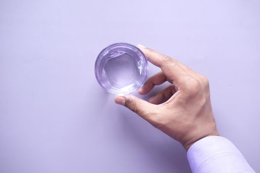 hand holding a glass of water on purple background .