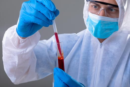 Caucasian male doctor wearing ppe suit holding test-tube. medical and healthcare technology concept during covid 19 coronavirus pandemic concept digitally generated composite image.