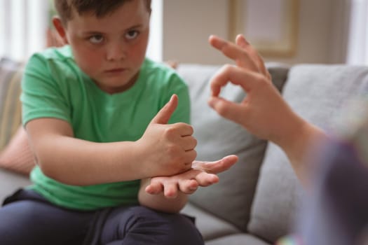 Two caucasian boys communicating using sign language while sitting on the couch at home. sign language learning concept