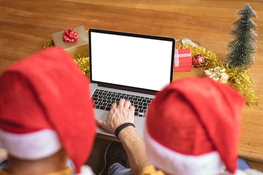 Rear view of father and son using laptop with copy space at home during christmas. social distancing during covid 19 pandemic at christmas time