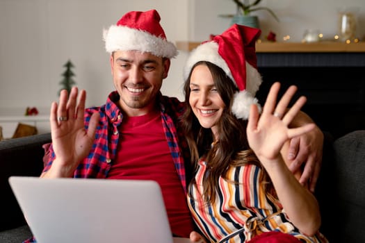 Happy caucasian couple wearing santa hats and having video call on laptop at christmas time. christmas, festivity and communication technology.
