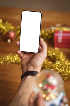 Hand holding smartphone with copy space against christmas gifts and decorations on wooden table. christmas festivity and celebration concept