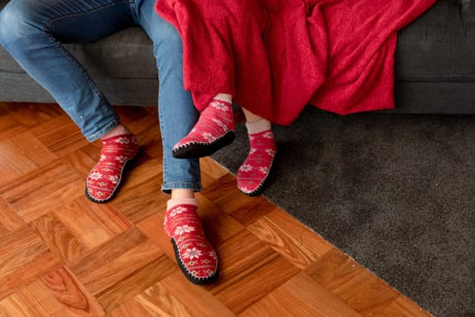 Legs of caucasian couple sitting on sofa with blanket in christmas socks. christmas, festivity and tradition at home.