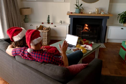 Back view of caucasian couple wearing santa hats, using laptop with copy space at christmas time. christmas, festivity and communication technology.