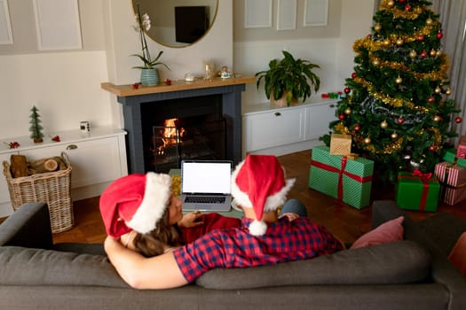 Back view of caucasian couple wearing santa hats, using laptop with copy space at christmas time. christmas, festivity and communication technology.