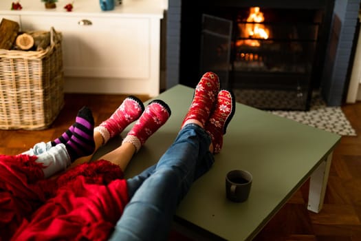 Feet of caucasian family wearing christmas socks and sitting on sofa at christmas time. family christmas time and festivity together at home.