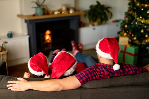 Back view of caucasian father and children wearing santa hats and christmas socks at christmas time. family christmas time and festivity together at home.