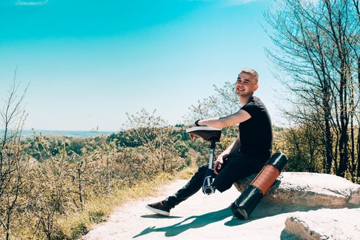 a man on a prosthetic leg travels the mountains. Dressed in black jeans and a T-shirt. sitting on a stone