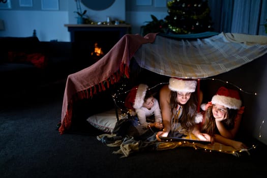 Happy caucasian mother, daughter and son wearing santa hats using tablet at christmas time. family christmas time and festivity together at home.