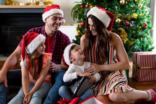 Happy caucasian family wearing santa hat, unpacking presents at christmas time. family christmas time and festivity together at home.