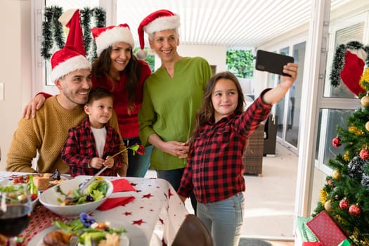 Caucasian multi generation family wearing santa hats taking selfie at christmas time. family christmas time and festivity together at home.