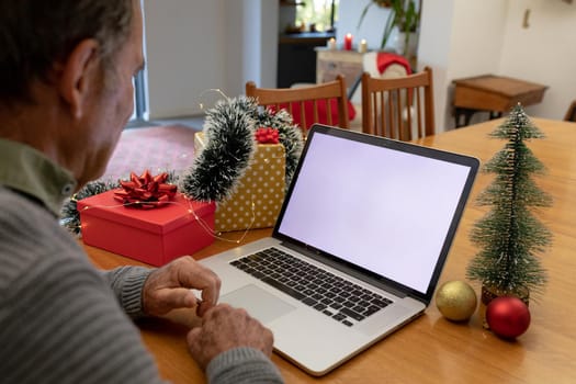 Caucasian senior man having video call on laptop with copy space at christmas time. christmas, festivity and communication technology at home.