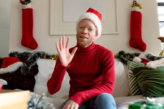 Albino african american man wearing santa hat making video call with christmas decorations. christmas, festivity and communication technology festivity and communication technology.