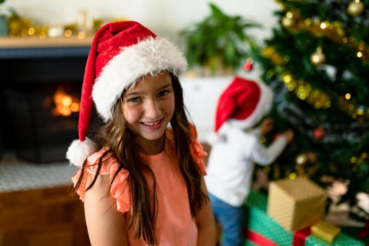 Happy caucasian girl wearing santa hat looking at camera at christmas time. childhood, chiristmas, festivity and tradition at home.