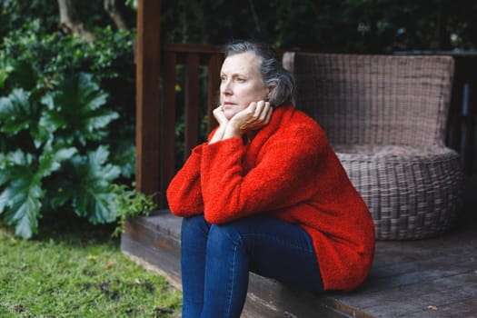 Thoughtful senior caucasian woman sitting and looking away in garden. retirement lifestyle, spending time alone at home.