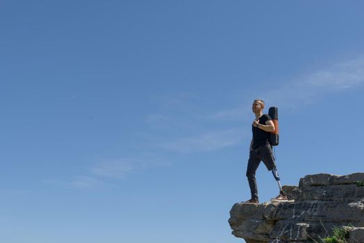 a man on a prosthetic leg travels the mountains. Dressed in black jeans and a T-shirt, he carrying mat.