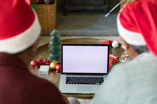 Two diverse senior female friends wearing santa hats using laptop with copy space at christmas time. christmas, festivity and communication technology.