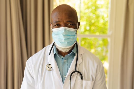Portrait of senior african american male doctor in face mask and lab coat. retirement and senior lifestyle during covid 19 pandemic concept.