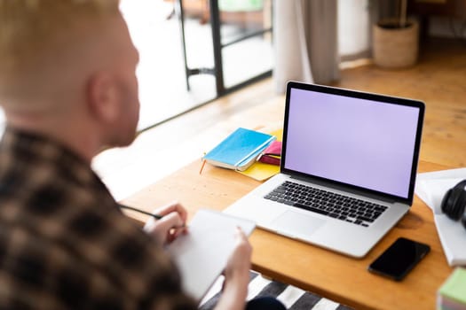 Albino african american man working from home using laptop with copy space. remote working using technology at home.