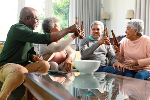 Two diverse senior couples sitting on sofa with beer and having fun. retirement lifestyle relaxing at home with technology.