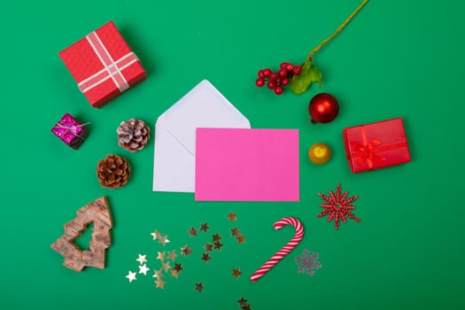Composition of envelopes with christmas decorations and baubles on green background. christmas, tradition and celebration concept.