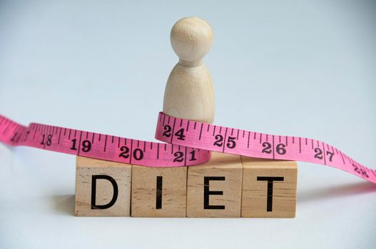 Diet text on wooden blocks with model wooden doll tied with measuring tape. Weight loss and fitness concept