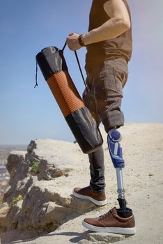 a man on a prosthetic leg travels the mountains. Dressed in black jeans and a T-shirt, he carrying mat.