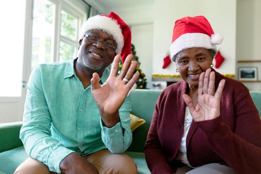 Happy african american senior couple wearing santa hats having video call at christmas time. christmas, festivity and communication technology.